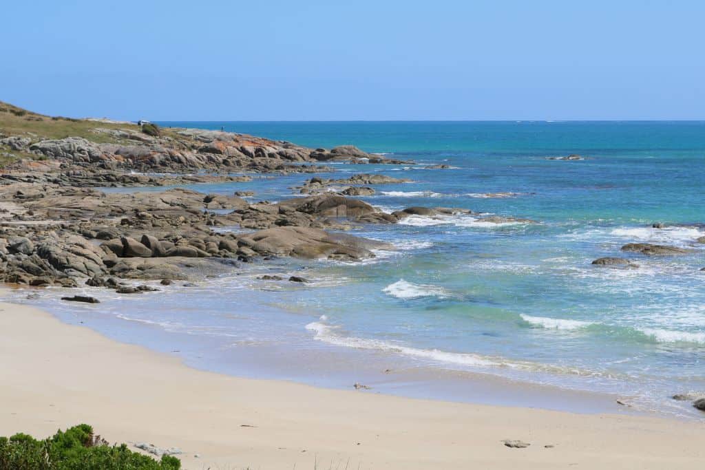 Waves gently rolling into sandy beach and rocky coast.