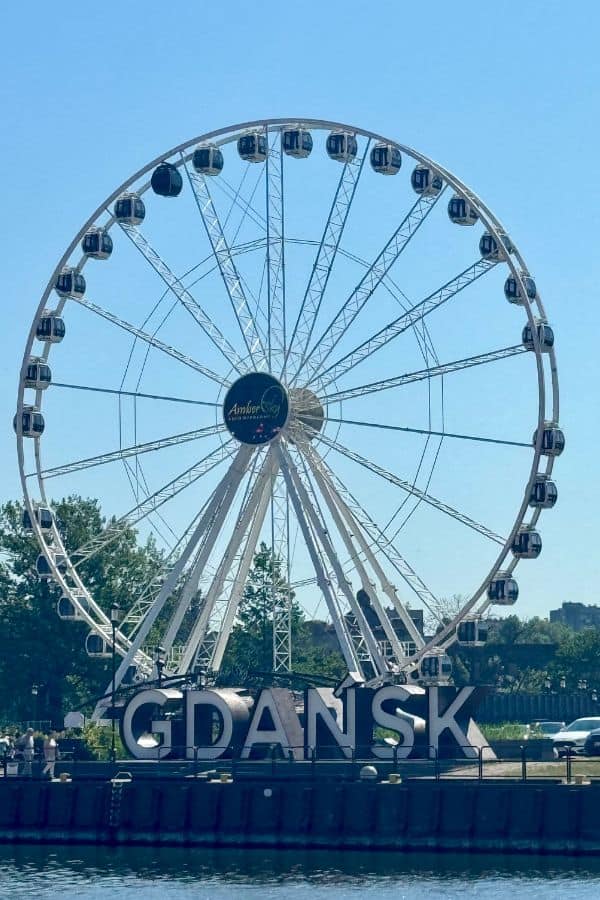 The Amber Sky Ferris wheel in Gdansk, Poland, with large white letters spelling 'GDANSK' at its base, set against a clear blue sky.