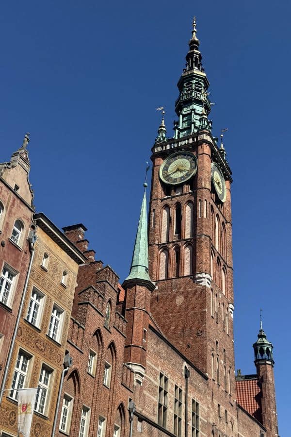 The Main Town Hall in Gdansk, Poland, featuring a tall clock tower with intricate architectural details against a clear blue sky.