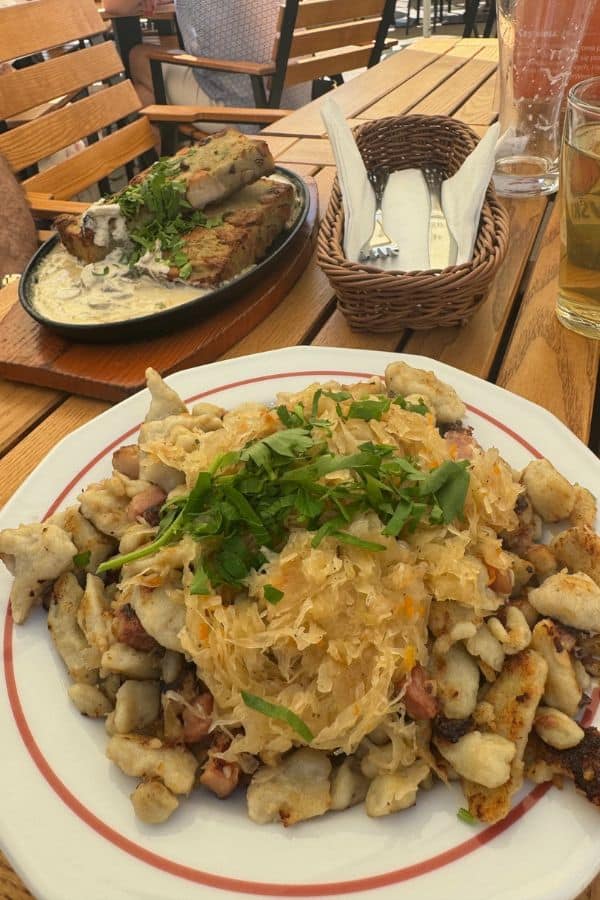A plate of fried dumplings topped with sauerkraut and herbs, and a dish of meat with creamy sauce at an outdoor restaurant in Gdansk.