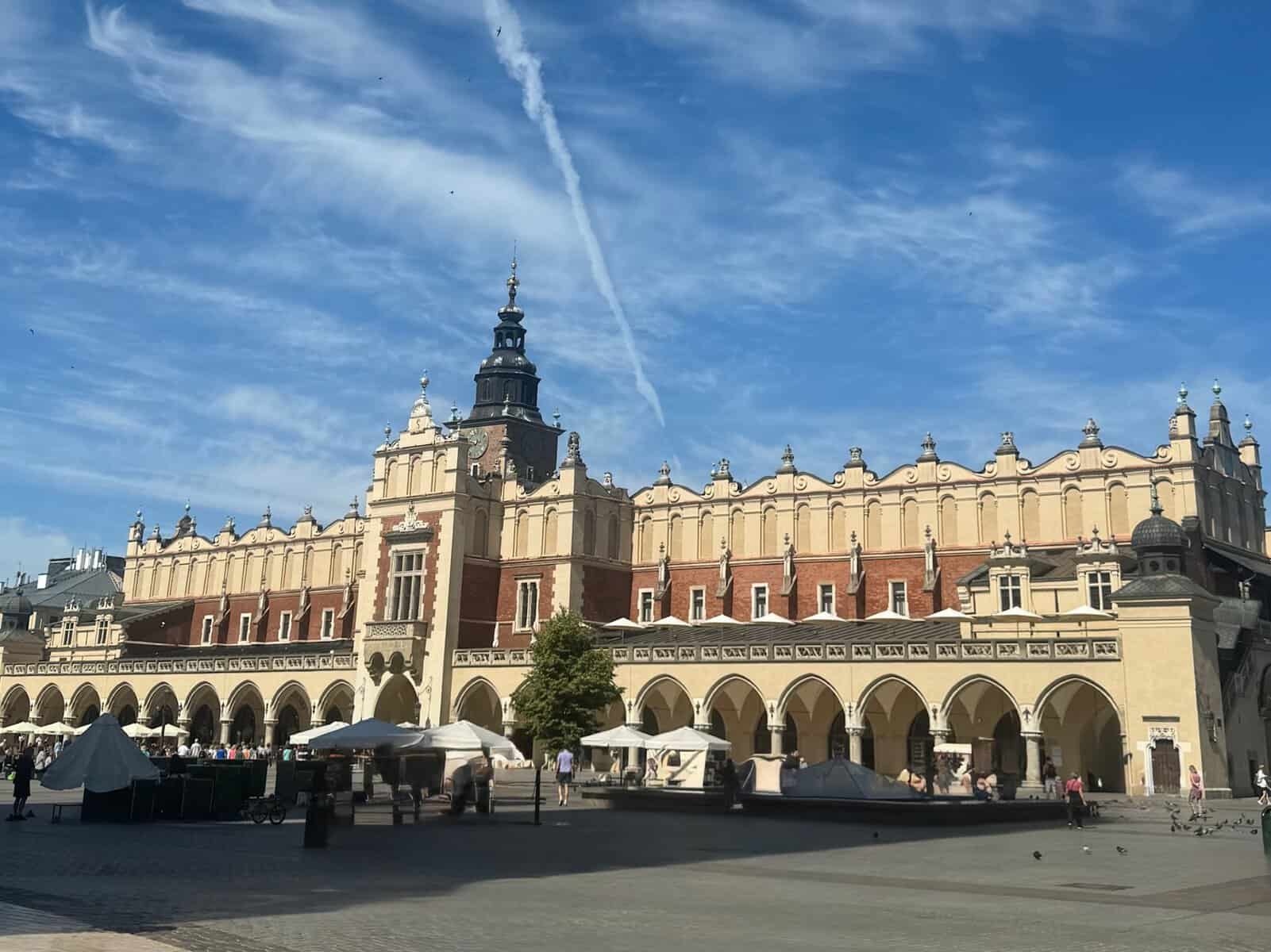 The Cloth Hall in Krakow's main square, featuring historic architecture with arches and a central tower under a blue sky.