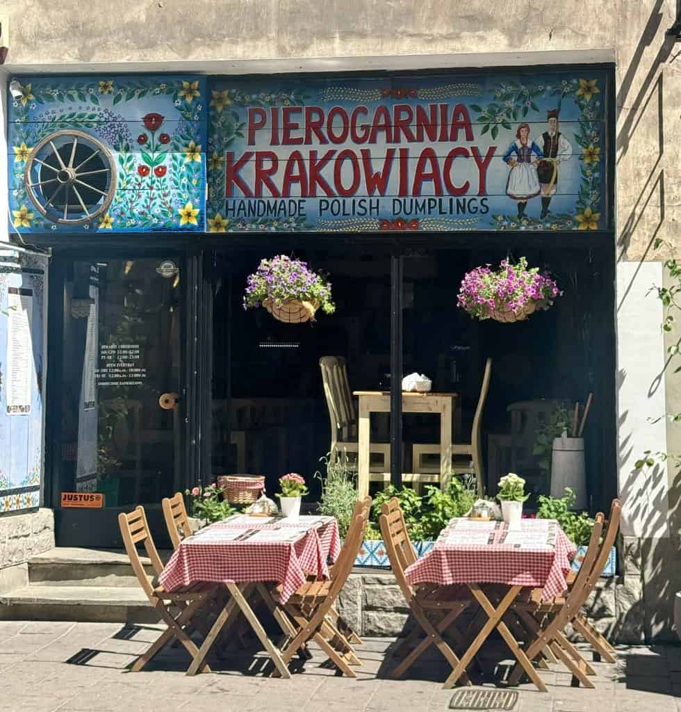 Cozy outdoor café in Krakow with patrons at sidewalk tables, colorful awnings, and historic buildings along a cobblestone street.