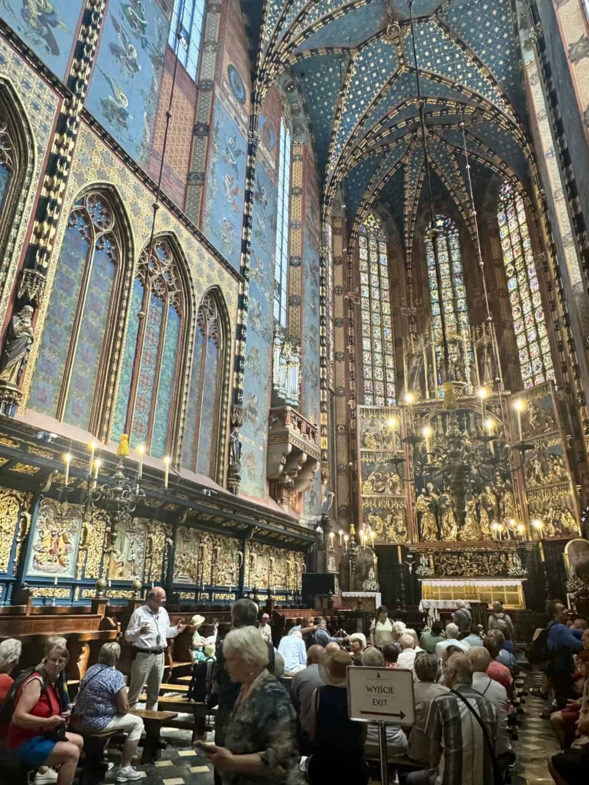 Interior of St. Mary's Basilica in Krakow with ornate decorations, stained glass windows, and visitors admiring the architecture.