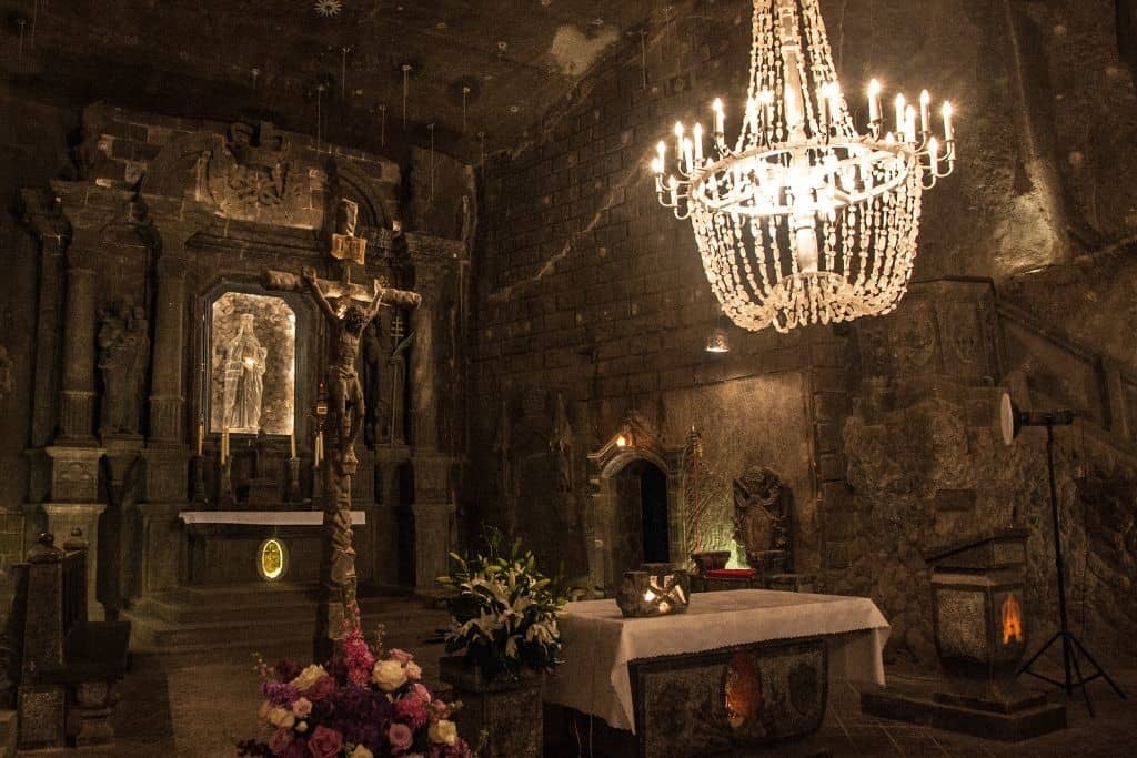 Grand hall inside Wieliczka Salt Mine with illuminated chandeliers, salt-carved walls, and intricate sculptures made entirely of salt.