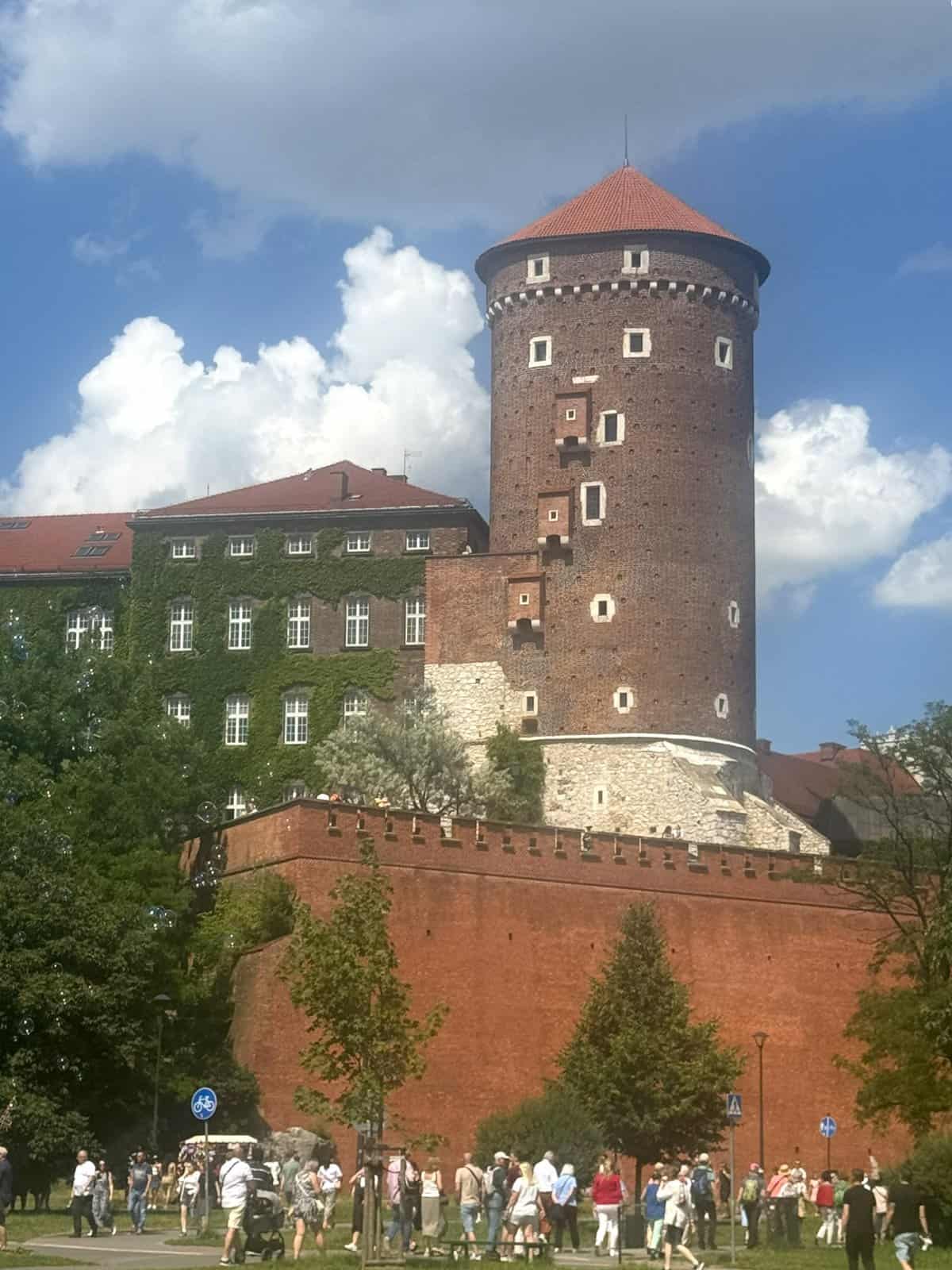 View of Wawel Castle from beside the Vistula River in Krakow, a majestic fortress atop a hill under clear sky.